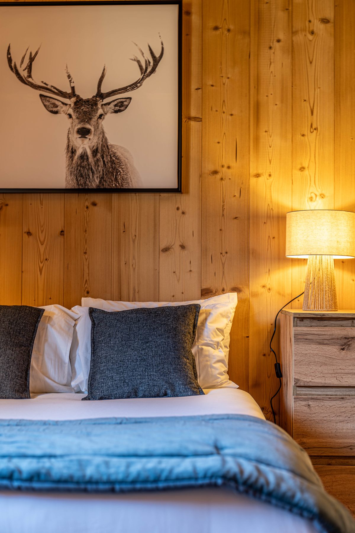 Chambre d'hôtel en bois clair, linge de lit blanc et coussins gris chiné