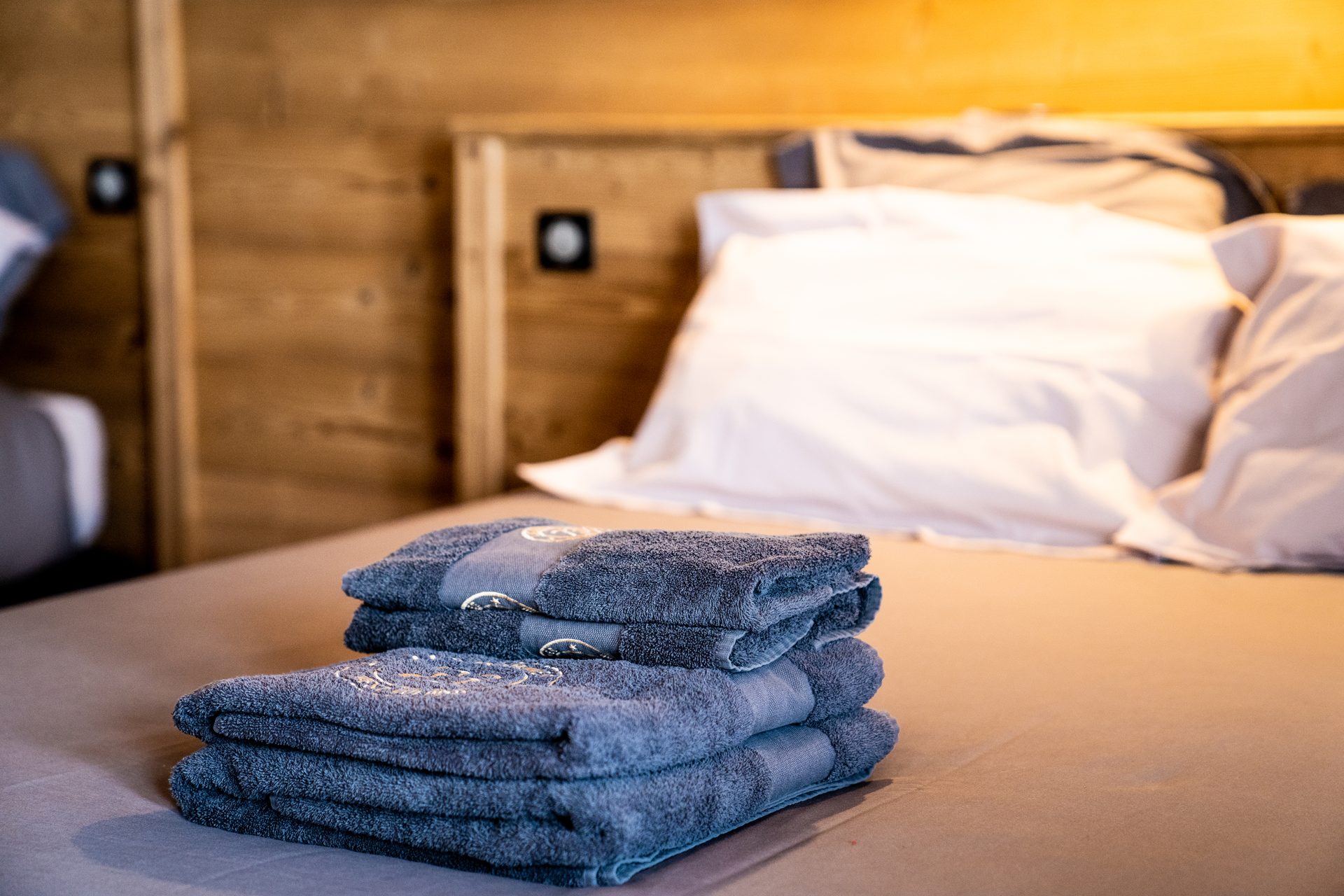 Serviettes brodées pliées sur un lit d'hôtel, ambiance chalet en bois